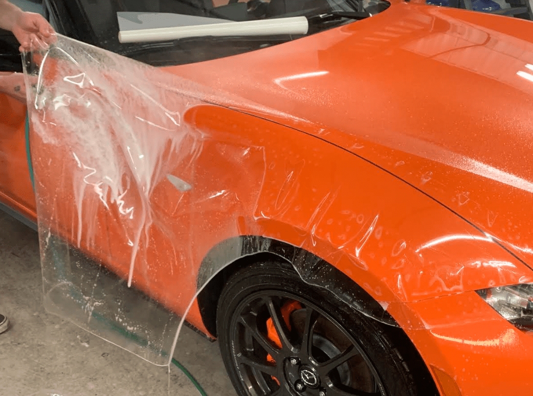Orange sports car getting paint protection film installed 